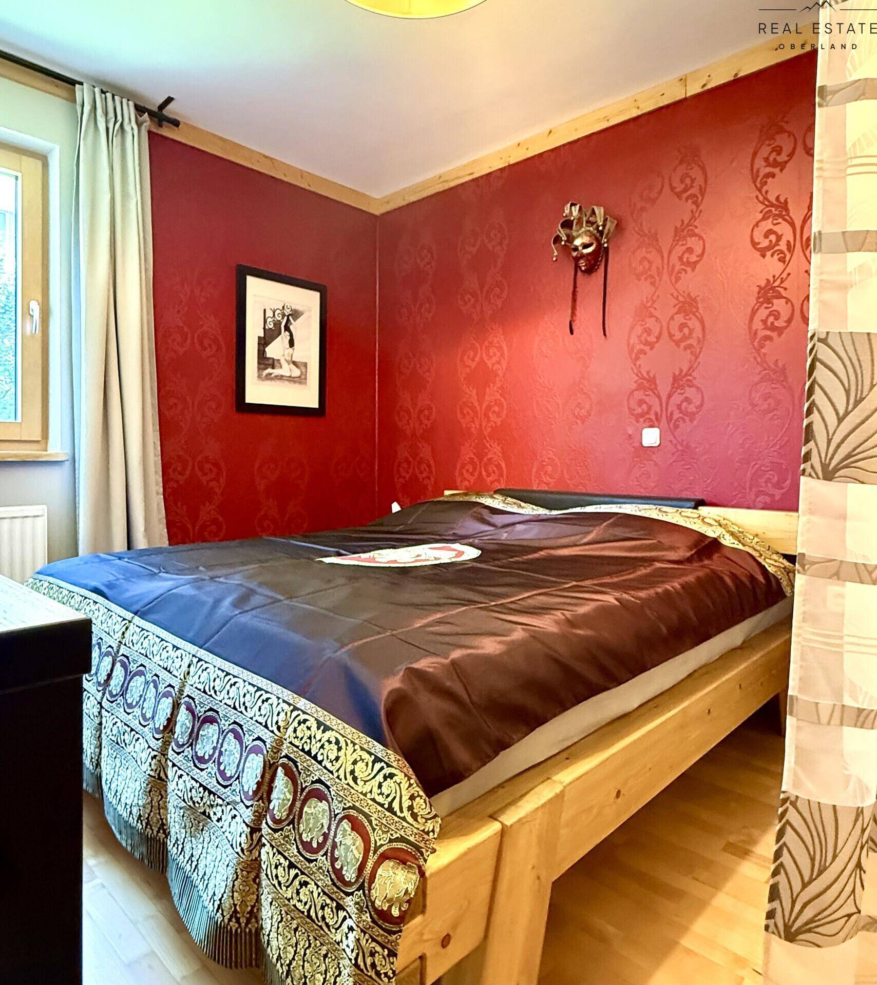 Schlafzimmer mit Holzbett, roter Tapete und traditioneller Bettwäsche.