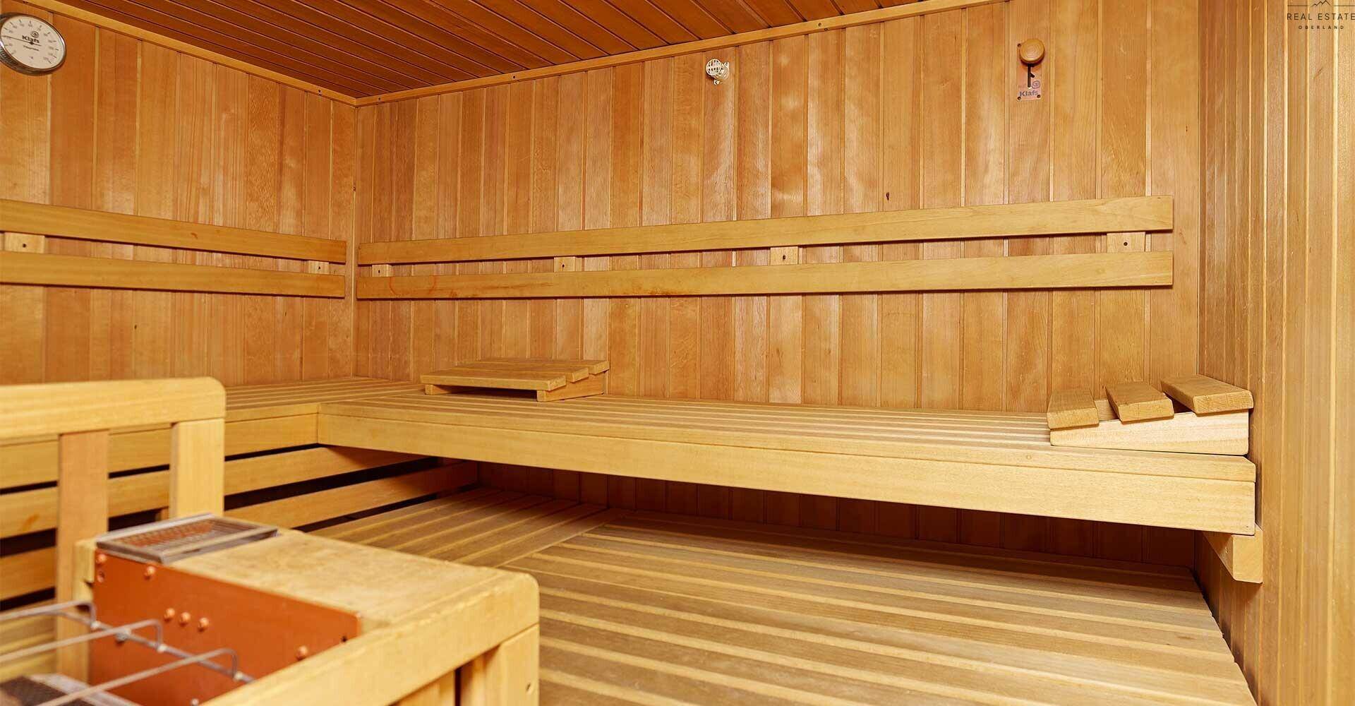 Geräumige Holzsauna mit mehreren Ebenen von Sitzbänken und einer Sanduhr an der Wand.
