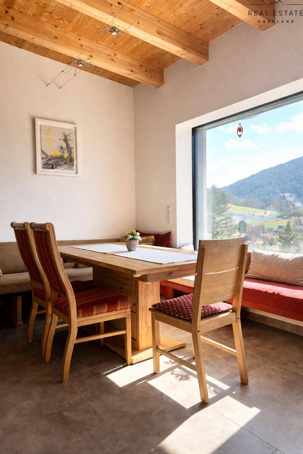 Gemütlicher Essbereich mit Holztisch und Sitzbank, großen Fenstern und Bergblick.