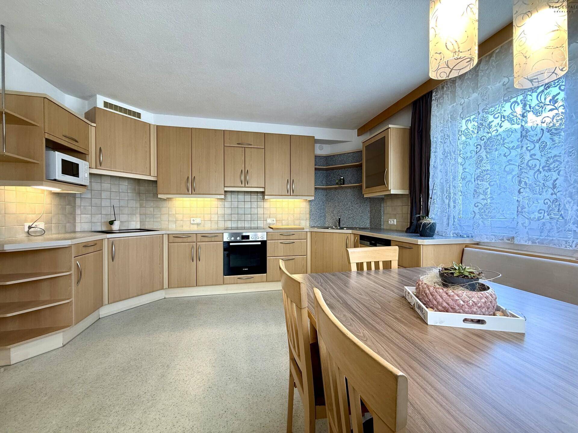 Helle Wohnküche mit Holzschränken, Essbereich und Blick auf den Garten durch das Fenster.