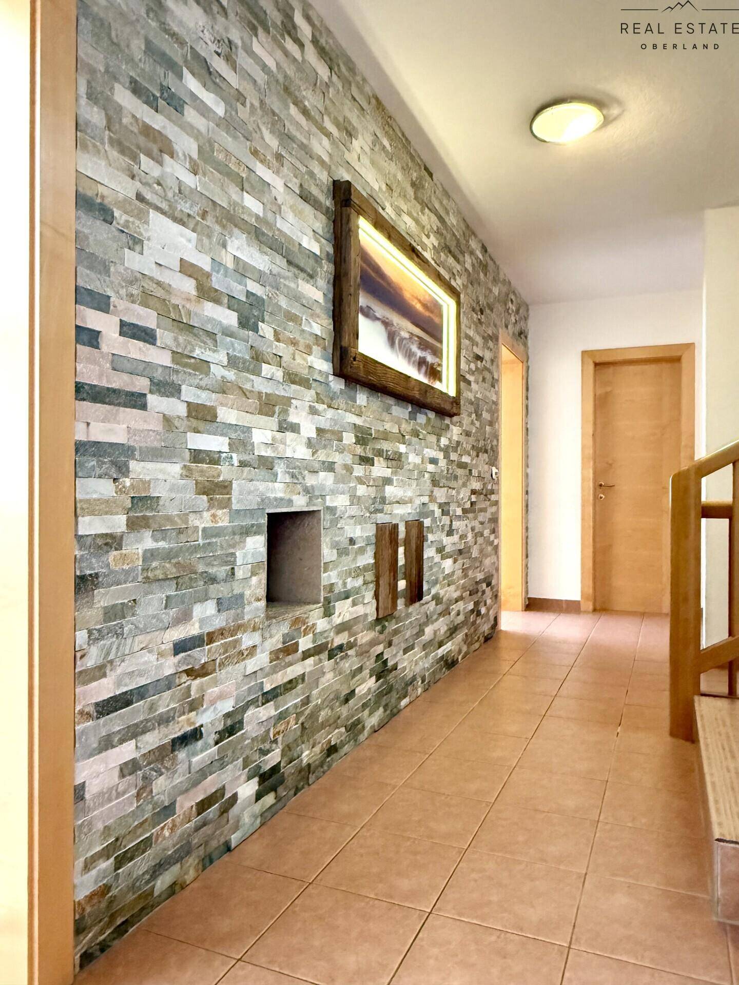 Heller Flur mit dekorativer Steinwand, Holzrahmen und Terrakotta-Fliesenboden.