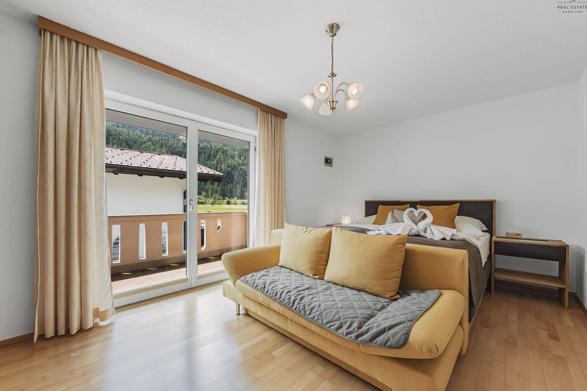 Helles Schlafzimmer mit Schlafsofa, Holzboden und direktem Zugang zum Balkon.