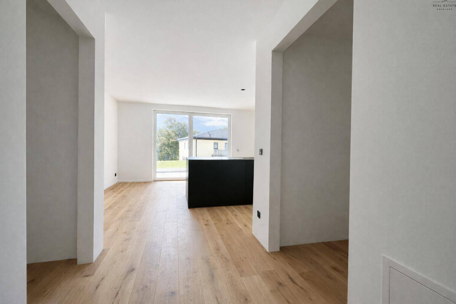 Heller Flur mit Holzboden, der zu einem offenen Wohnbereich mit großen Fenstern führt.