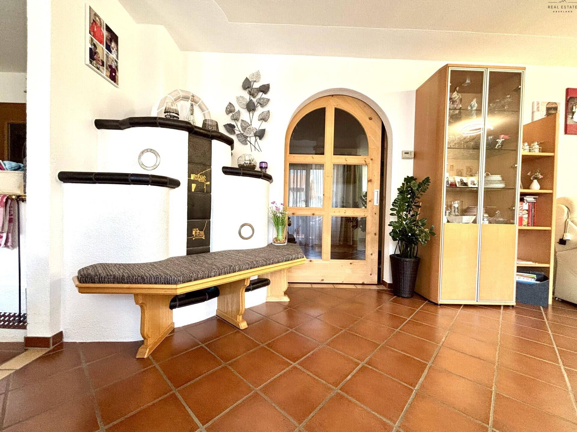 Geräumiger Wohnbereich mit traditionellem Kachelofen, Vitrine und Terrakottafliesen, hell und einladend.
