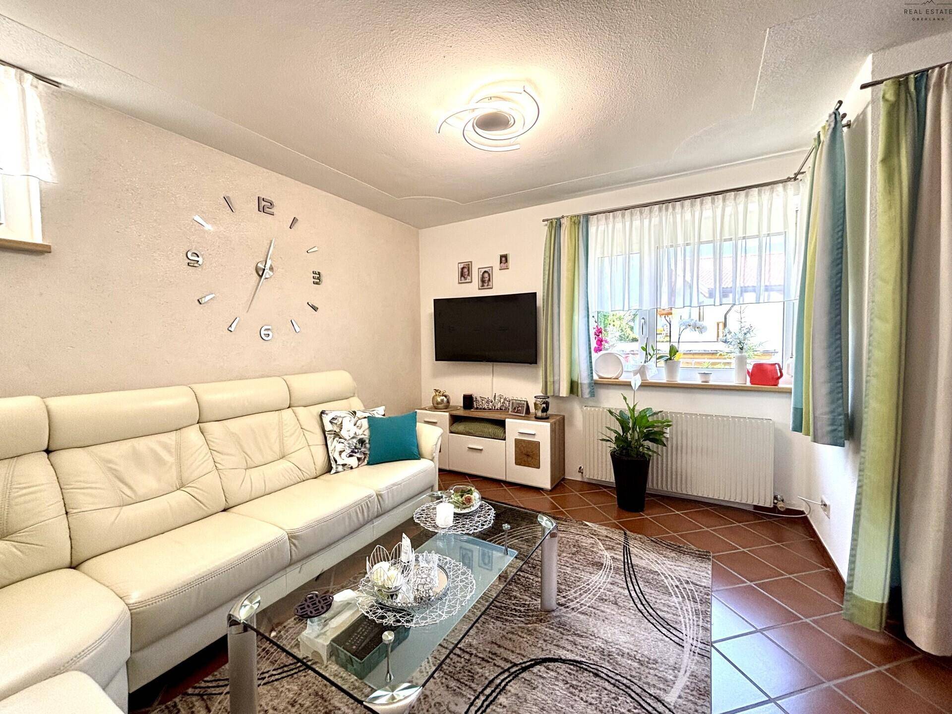 Helles Wohnzimmer mit beigem Ledersofa, Glascouchtisch und Terrakottafliesen, modern eingerichtet.