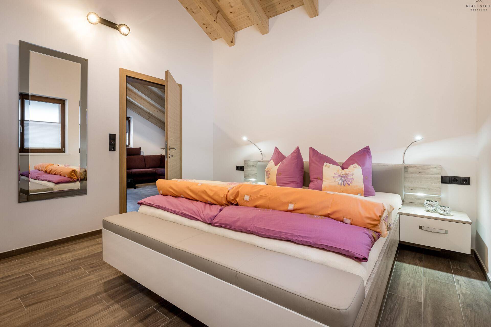 Gemütliches Schlafzimmer mit Doppelbett, Holzbalkendecke und Zugang zum Wohnbereich.