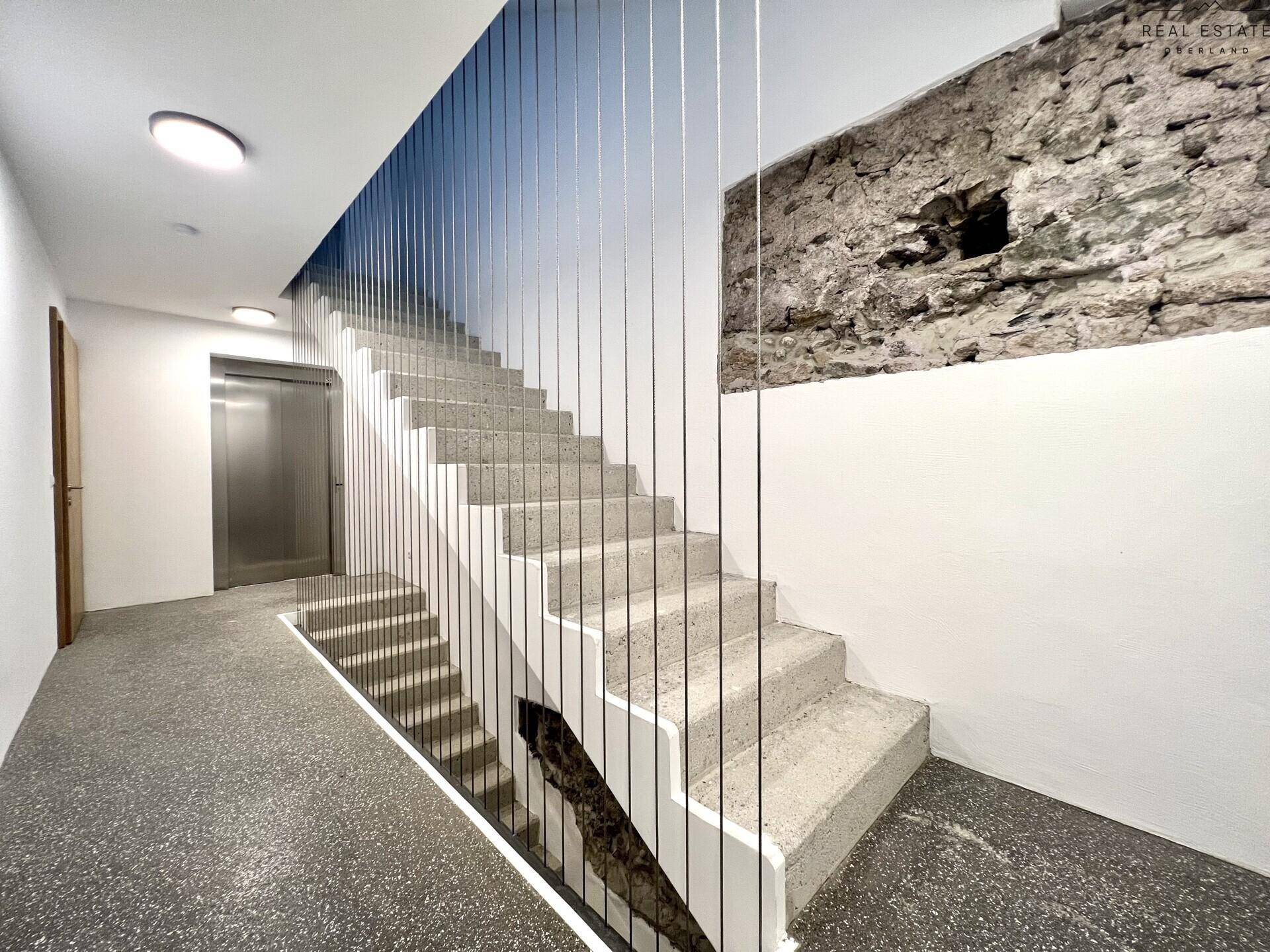 Modernes Treppenhaus mit Aufzug und einer stilvollen Kombination aus Stein und Metall.