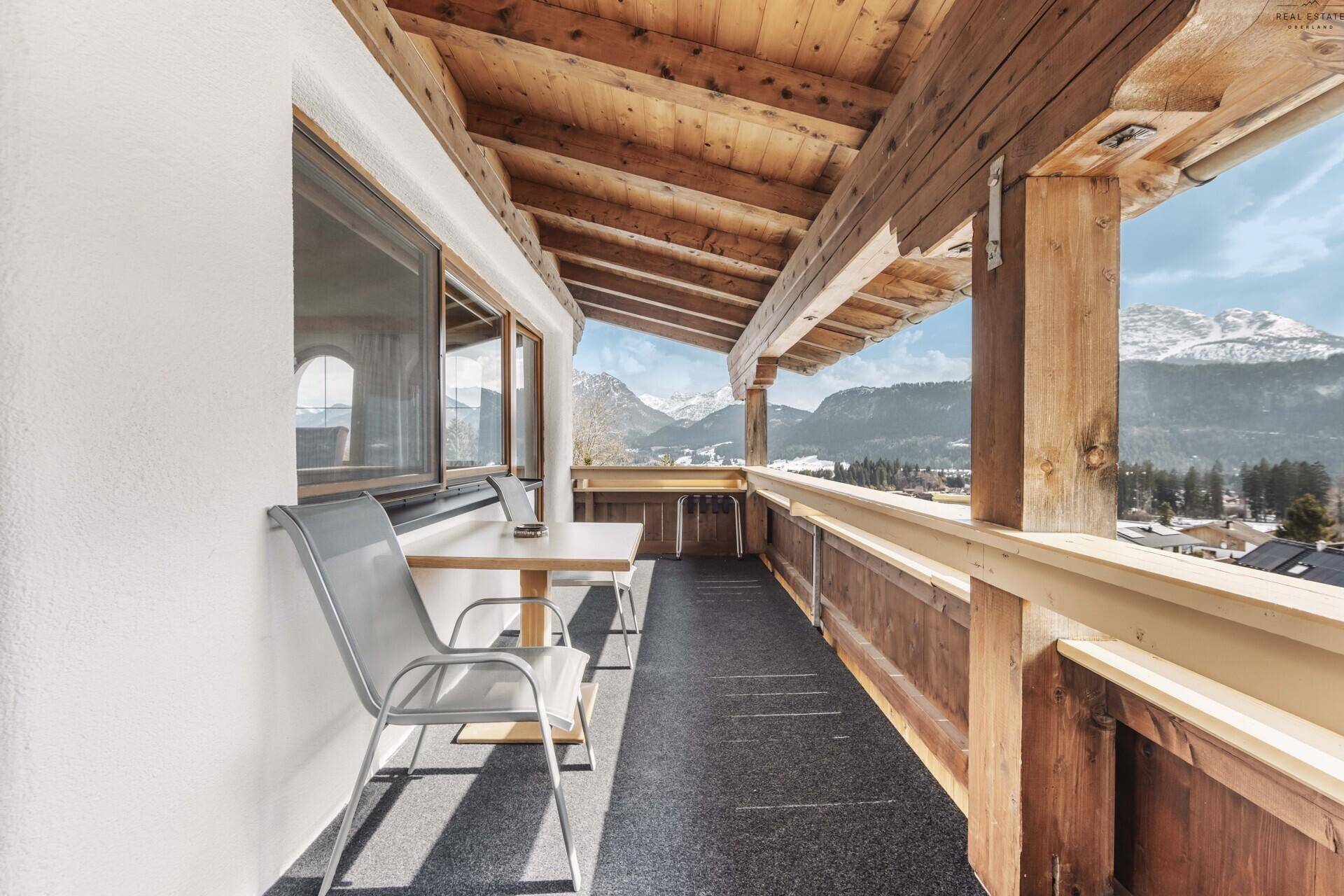 Sonniger Balkon mit Holzelementen, Tisch und Stühlen, ideal für entspannte Stunden mit Bergblick.