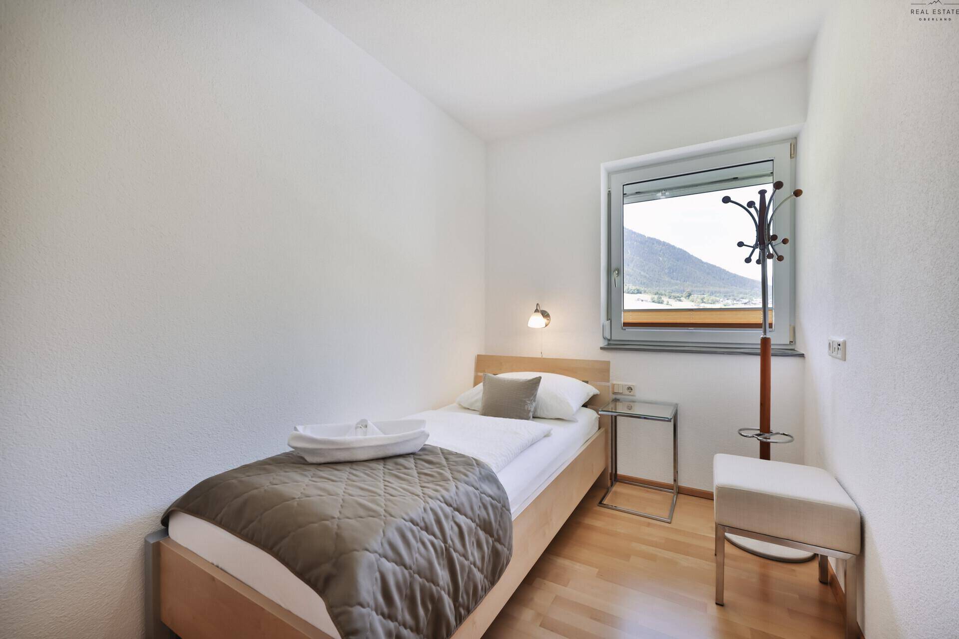 Kleines Schlafzimmer mit Einzelbett, Holzboden und Fenster mit Bergblick.