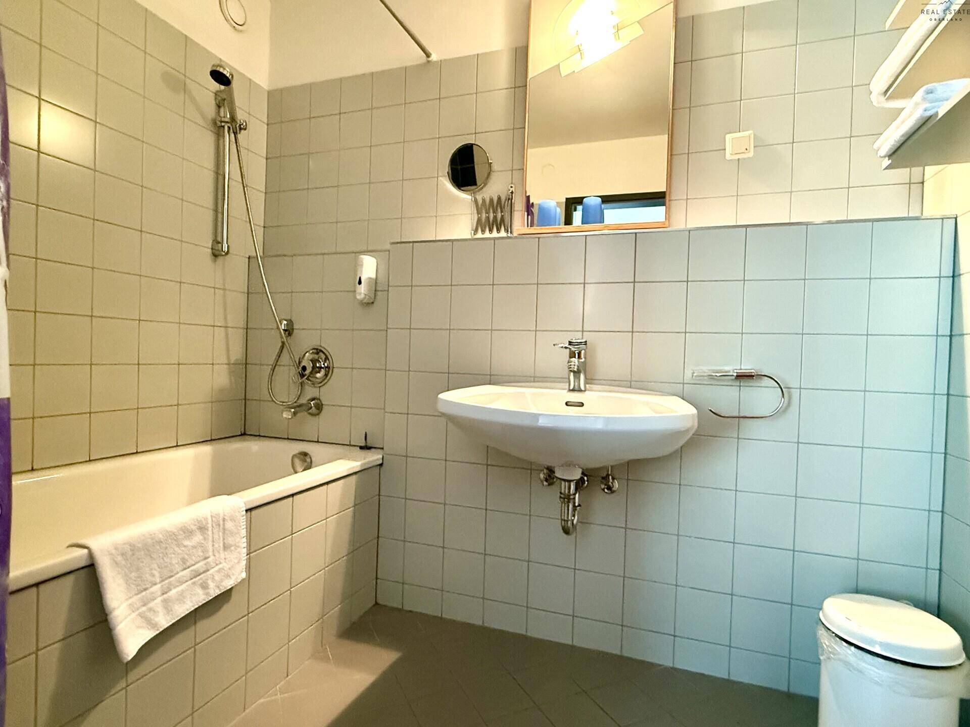 Badezimmer mit Badewanne, Waschbecken und hellen Fliesen an den Wänden.