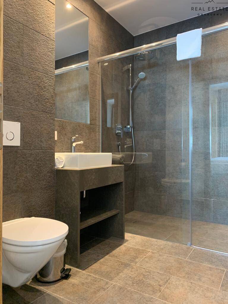 Modernes Badezimmer mit ebenerdiger Dusche, Einzelwaschbecken und Wand-WC.