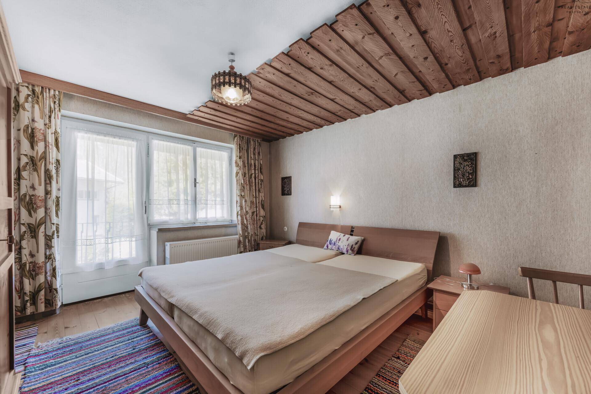 Gemütliches Schlafzimmer mit Doppelbett, Holztisch und dekorativer Holzdecke.