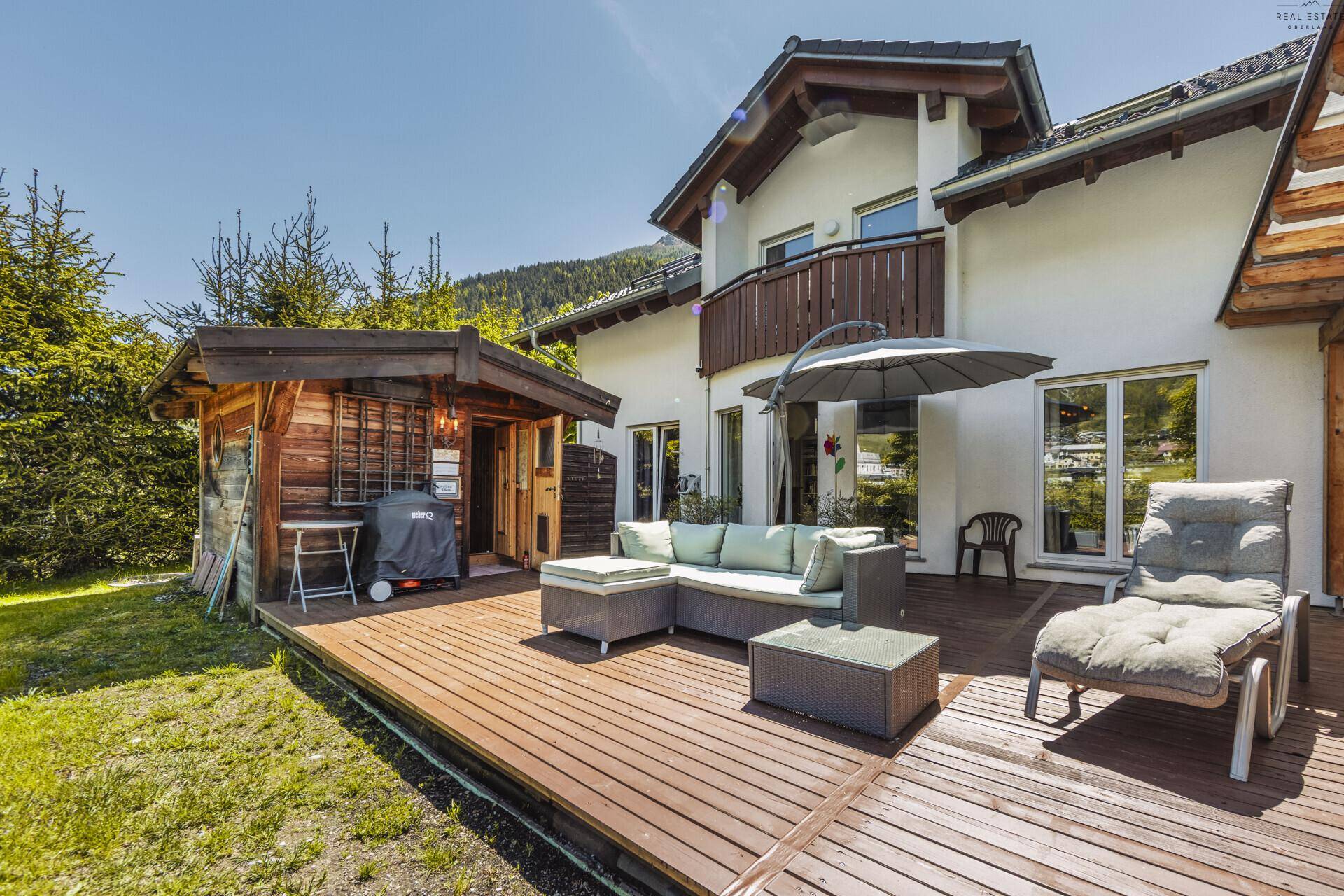 Hausfassade mit weitläufiger Holzterrasse, Gartenmöbeln und einem charmanten Holzschuppen.