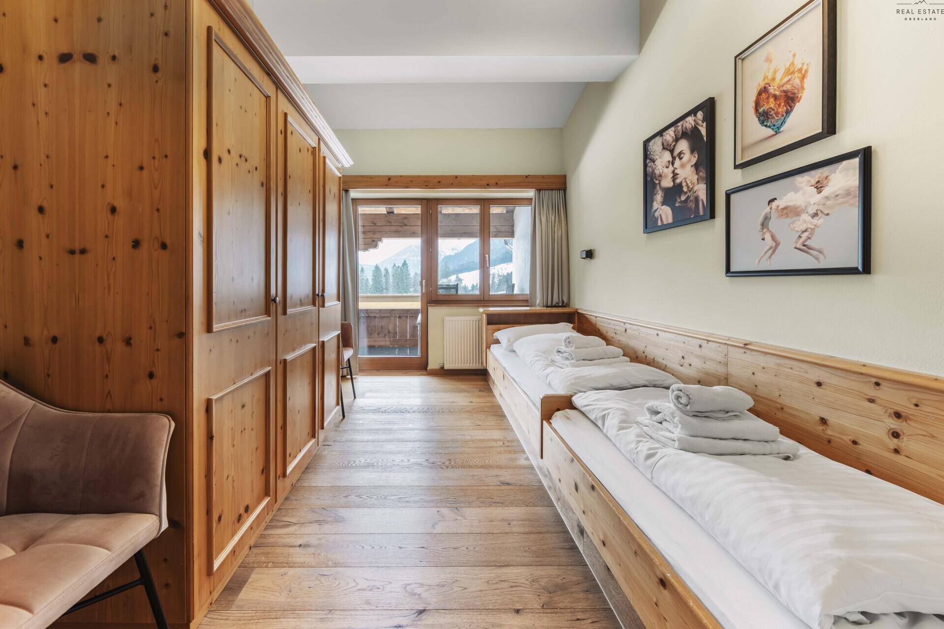 Schlafzimmer mit zwei Einzelbetten, Holzboden und Zugang zu einem Balkon.