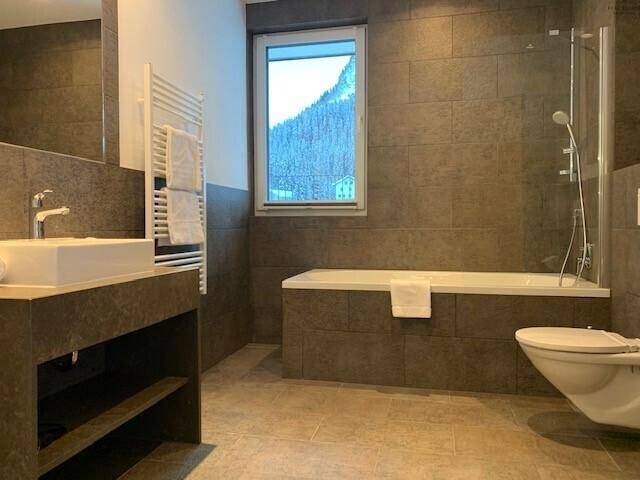 Modernes Badezimmer mit Badewanne, Dusche, Einzelwaschbecken und Fenster mit Bergblick.