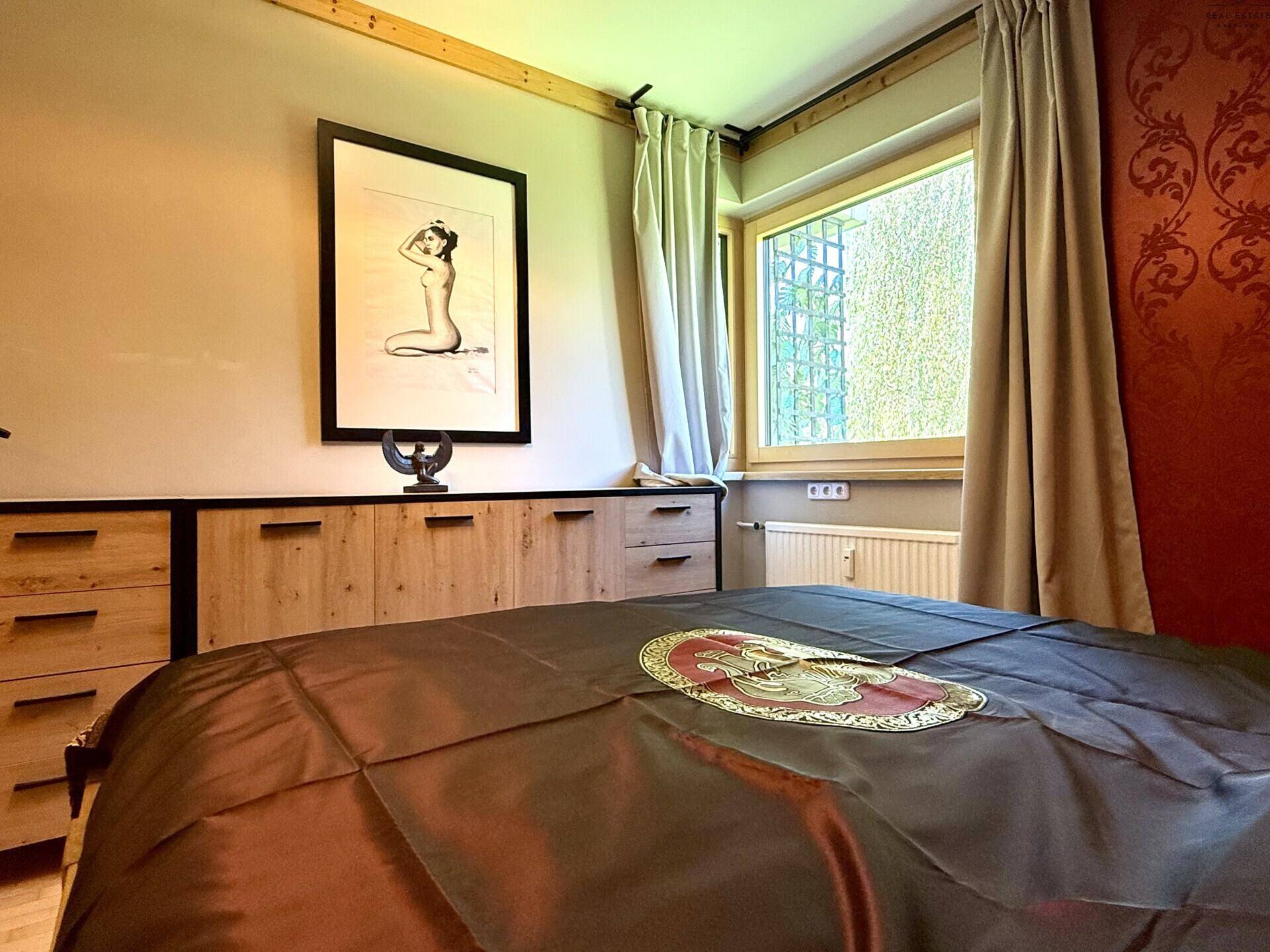 Schlafzimmer mit Holzbett, Fenster und Blick ins Grüne.