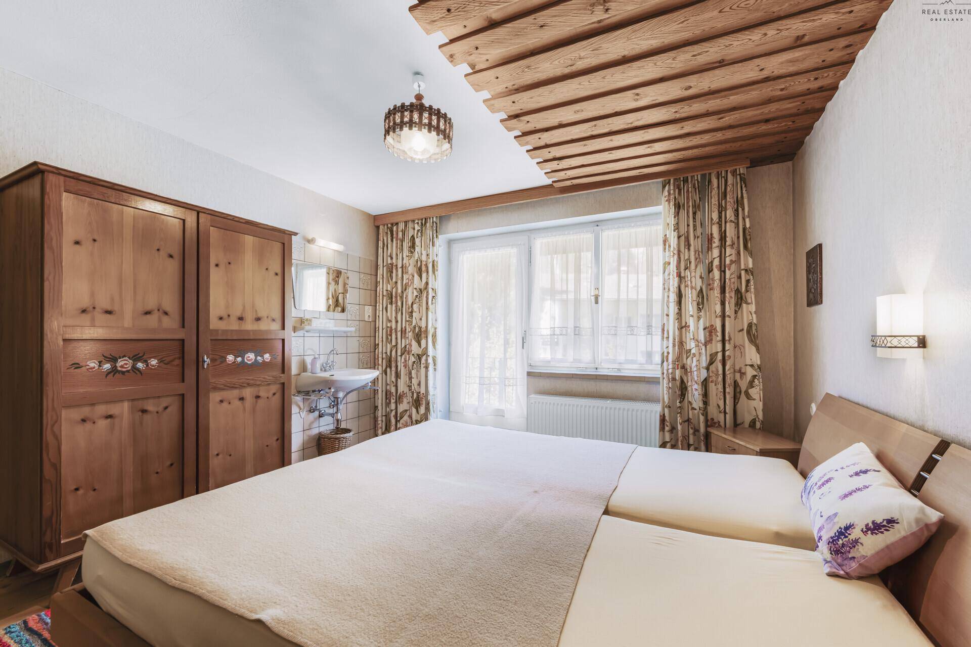 Schlafzimmer mit Doppelbett, großem Holzschrank und integriertem Waschbecken.