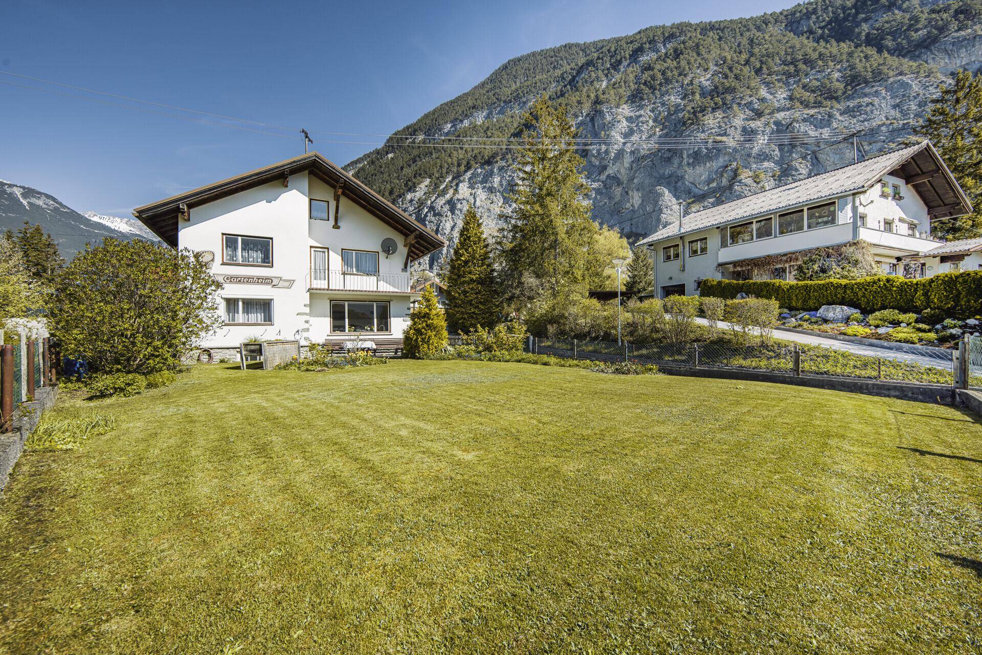 Gepflegter Garten mit großer Rasenfläche vor dem Haus und Bergblick.