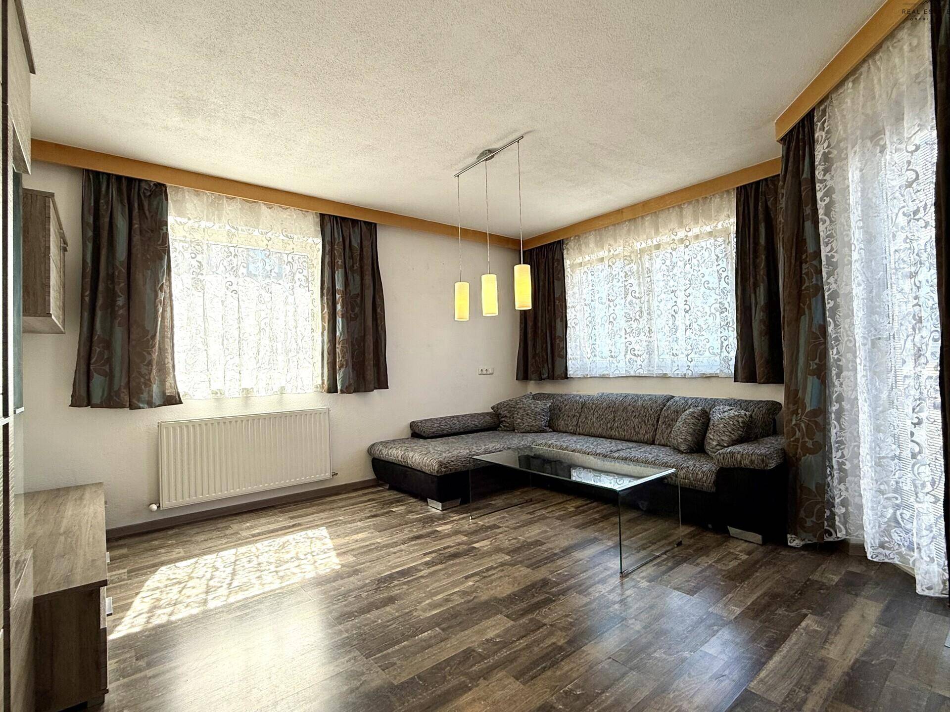 Helles Wohnzimmer mit großem Ecksofa, Holzboden und Fenster mit Vorhängen.