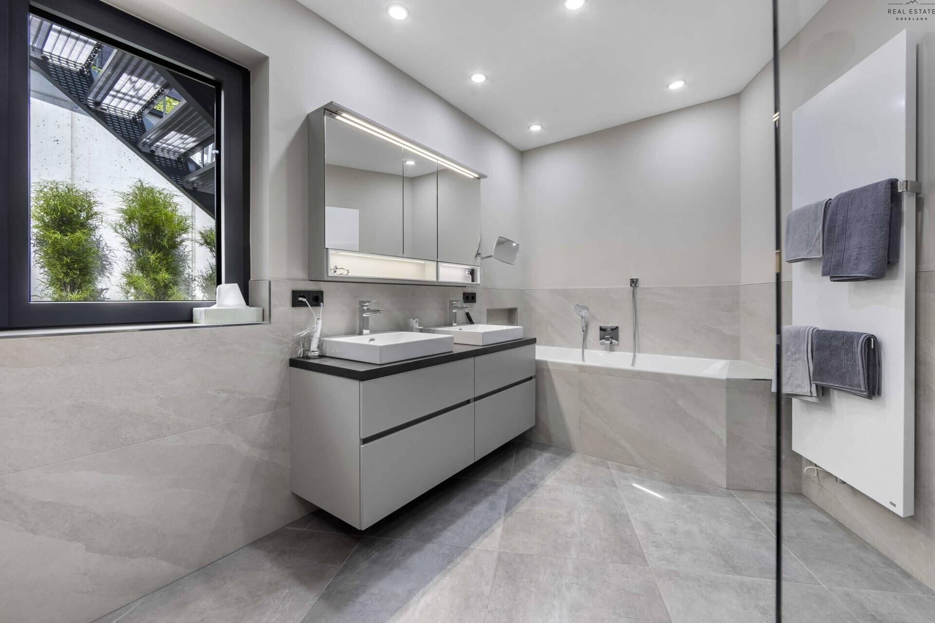 Stilvolles Badezimmer mit Doppelwaschbecken, Badewanne, beheiztem Handtuchhalter und Fenster.