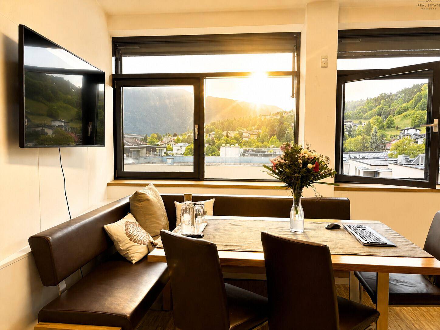 Ess- oder Pausenbereich mit Ledersitzbank, Tisch und Fenstern mit Bergblick bei Sonnenuntergang.