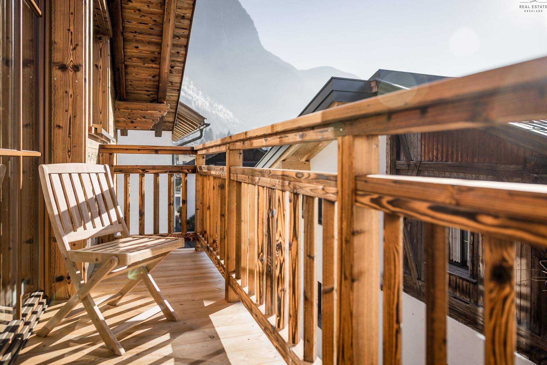 Sonniger Holzbalkon mit einem Stuhl und Blick auf die umliegende Berglandschaft.