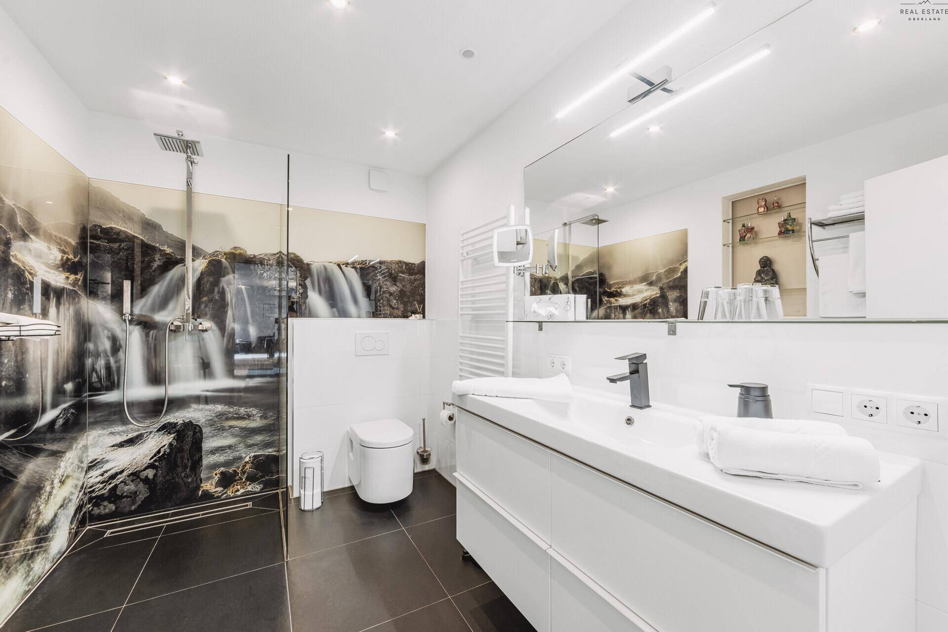 Modernes Badezimmer mit ebenerdiger Dusche, Wand-WC und großem Waschtisch mit Einzelwaschbecken.