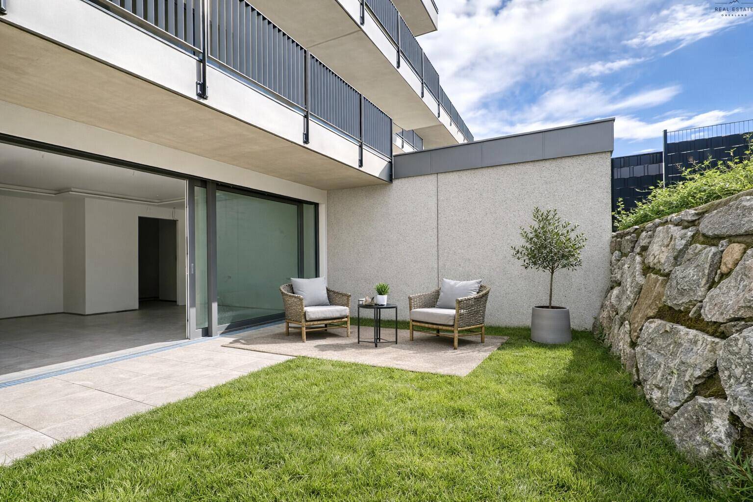 Gemütliche Terrasse mit Sitzgelegenheiten, Rasenfläche und Blick auf das moderne Gebäude.