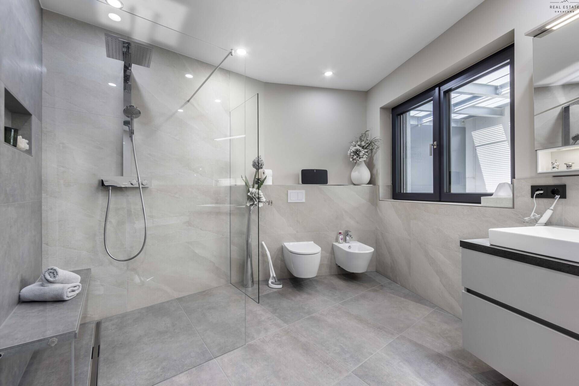 Elegantes Badezimmer mit großer begehbarer Dusche, WC, Bidet und Fenster.