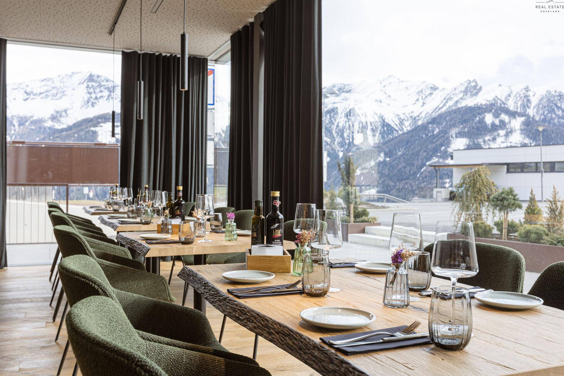 Nahaufnahme der gedeckten Tische im Essbereich mit Panoramablick auf die schneebedeckten Berge durch große Fenster.