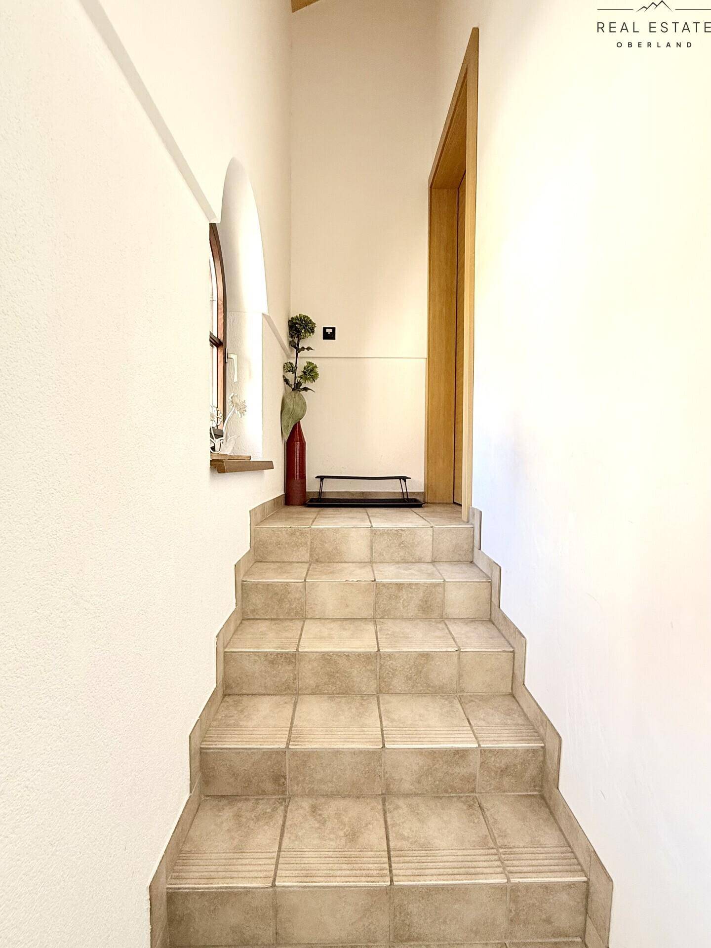 Treppenaufgang mit Fliesenboden und Bogenfenster, führt in die obere Etage.