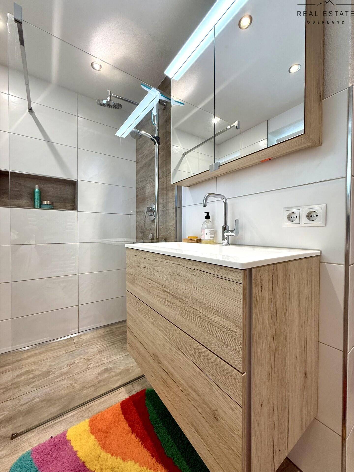 Modernes Badezimmer mit begehbarer Dusche, Holzwaschtisch und großem Spiegelschrank.
