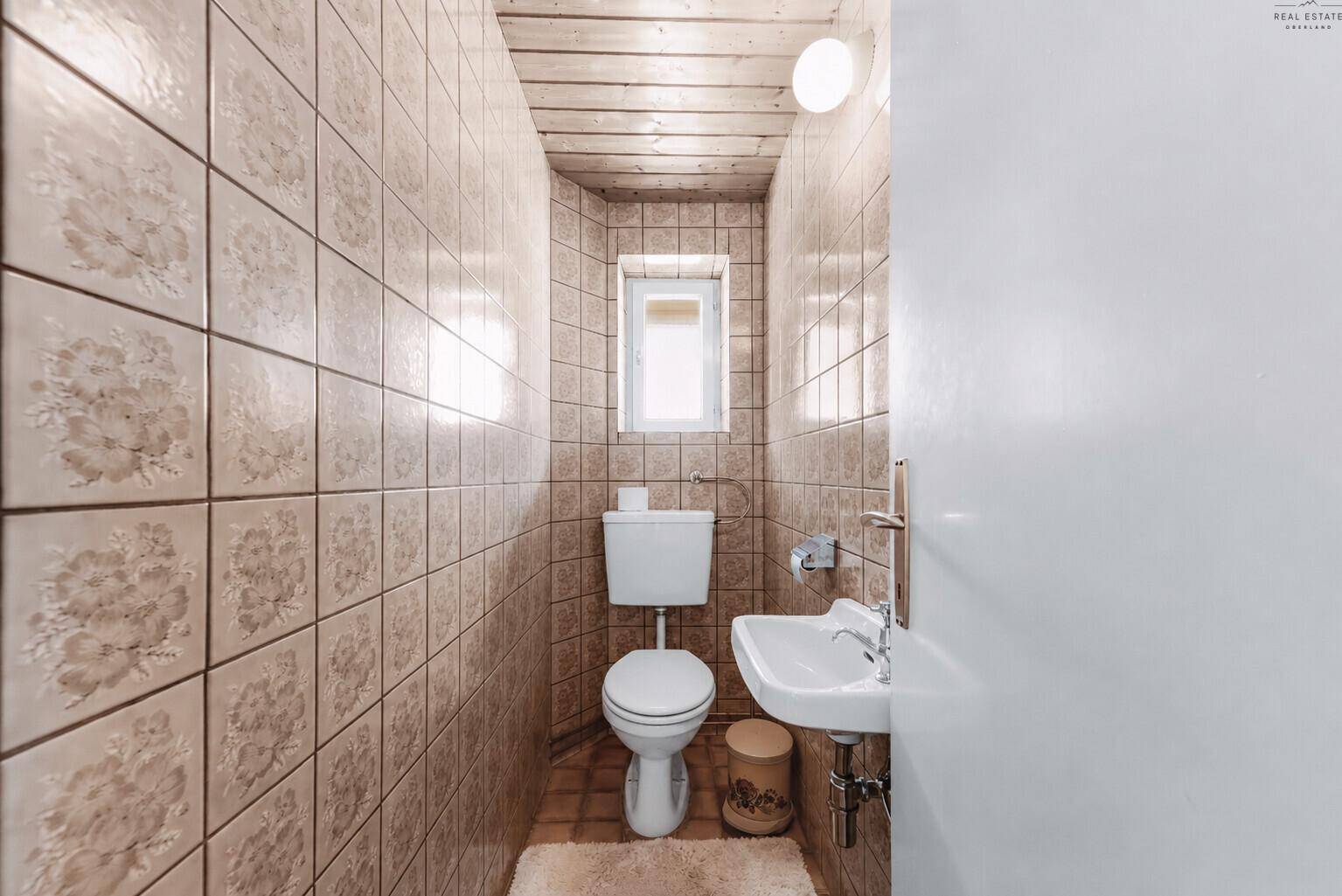 Separates WC mit kleinem Waschbecken und Fenster, komplett gefliest in warmen Farbtönen.