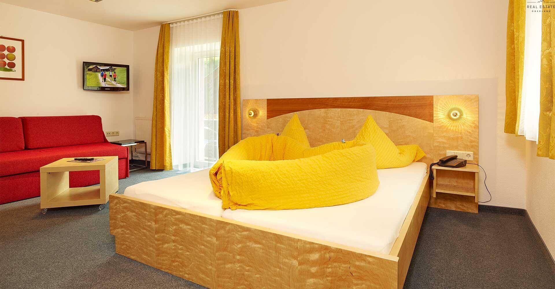 Geräumiges Schlafzimmer mit Doppelbett, rotem Sofa und gelber Bettwäsche, hell und einladend.