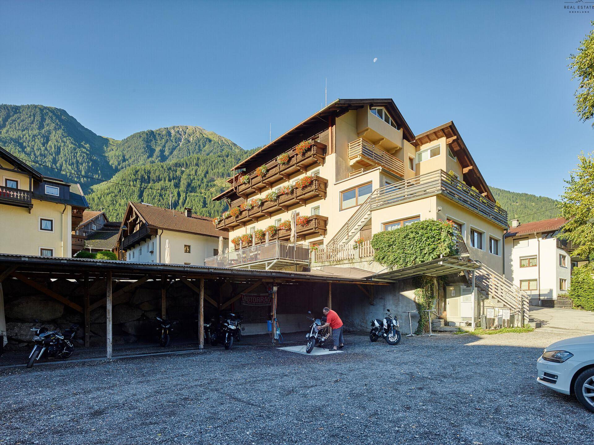 Außenansicht eines Gebäudes mit überdachtem Parkplatz für Motorräder und Blick auf die Berge.
