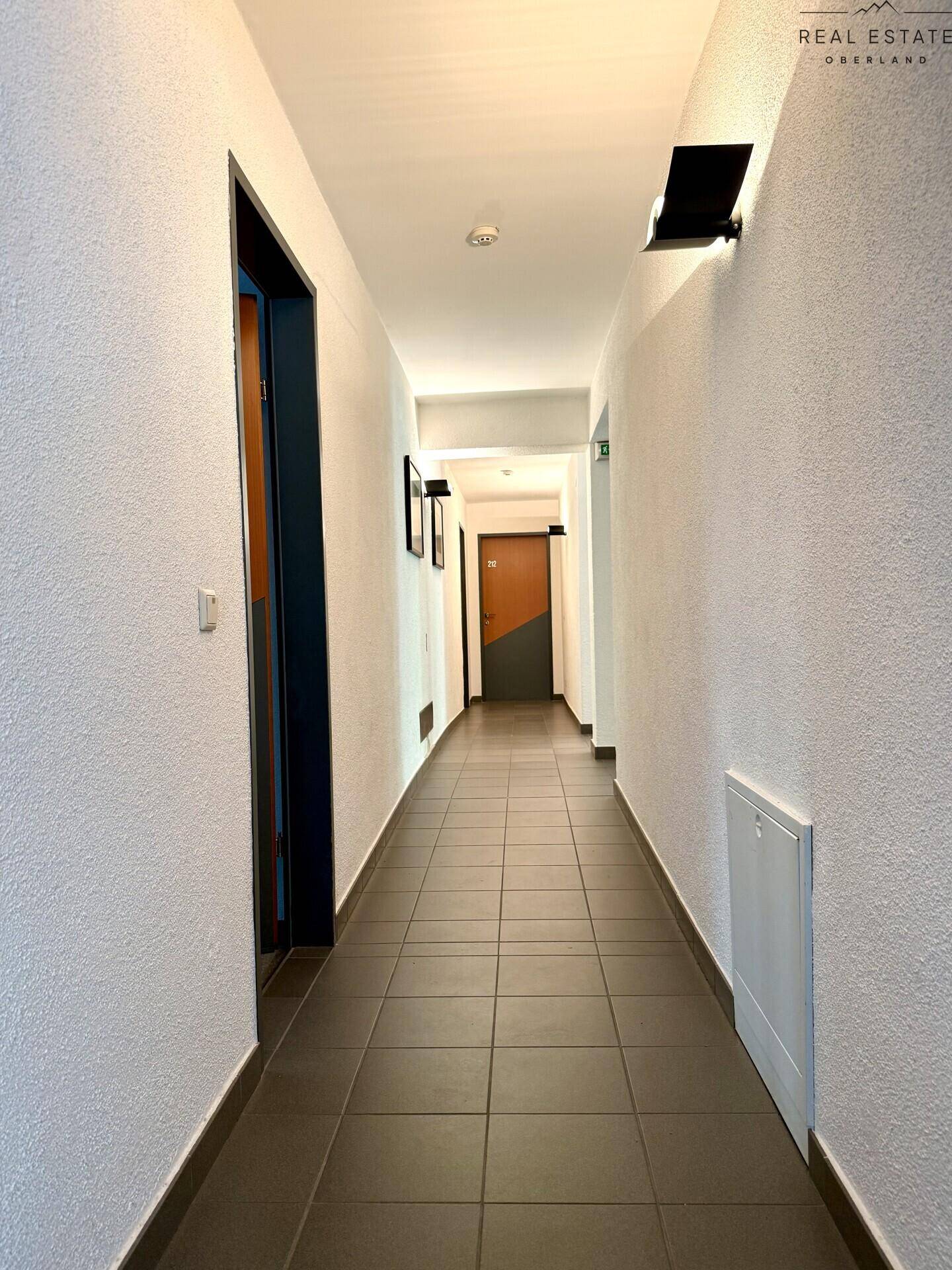 Langer Flur mit Fliesenboden und Türen zu verschiedenen Zimmern, gut beleuchtet.