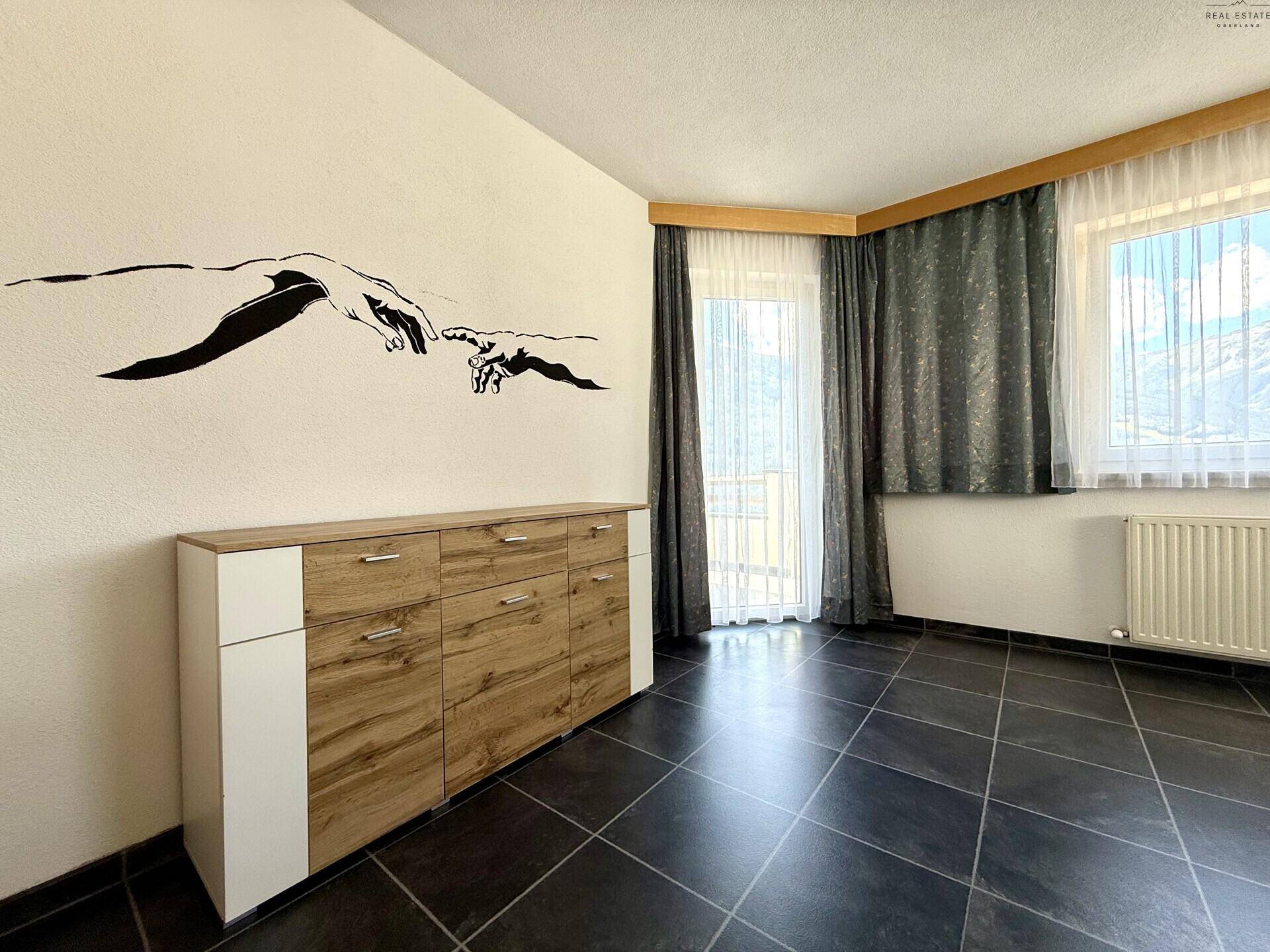 Schlafzimmer mit dunklem Fliesenboden, Sideboard und Fenstern mit Bergblick und Vorhängen.