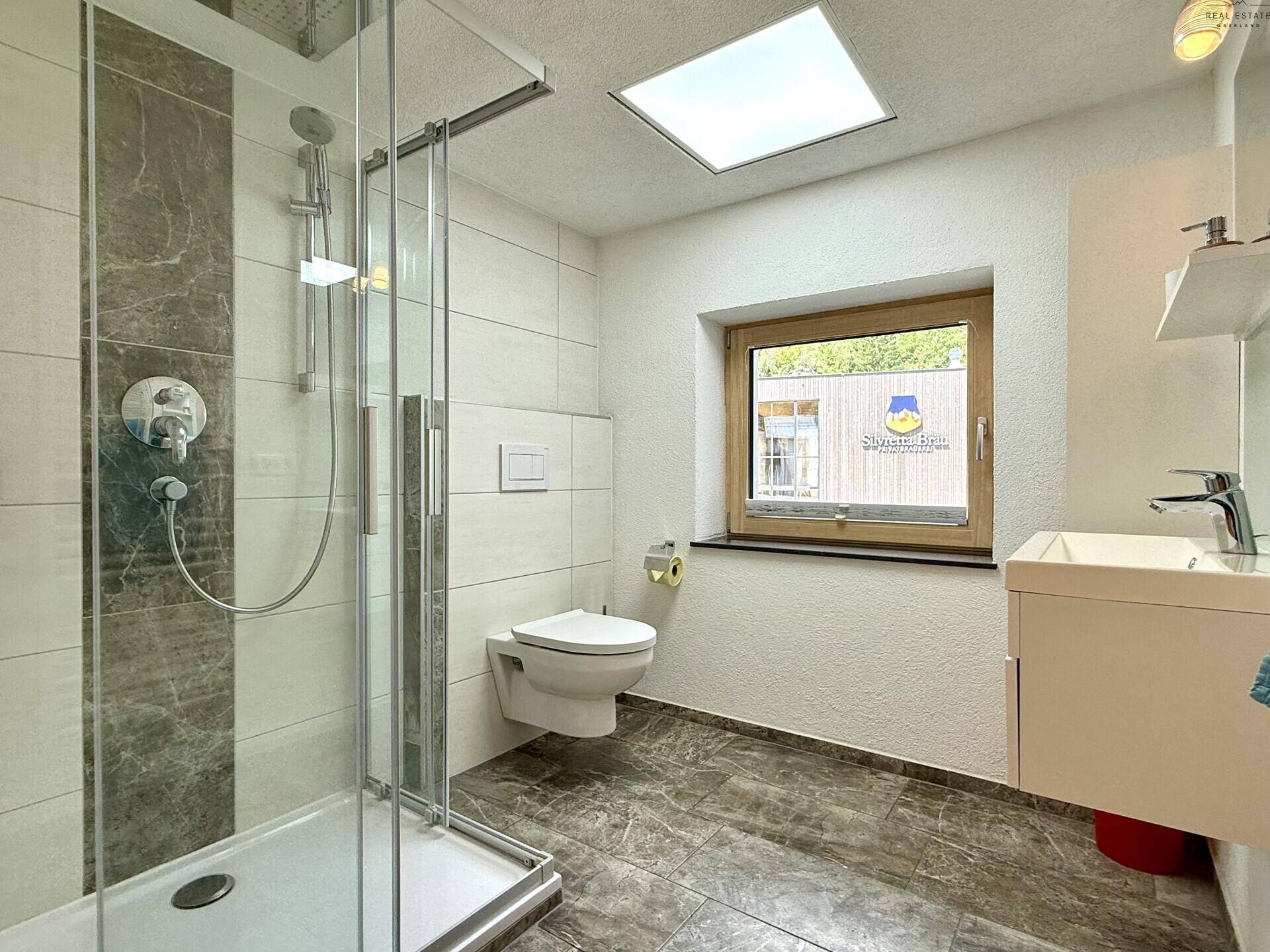 Helles Badezimmer mit Duschkabine, wandhängendem WC und großformatigen Fliesen.