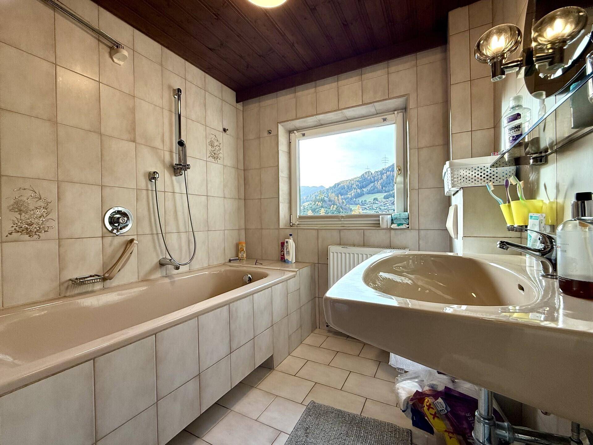 Traditionelles Badezimmer mit Badewanne, Waschbecken und Fenster mit Bergblick.