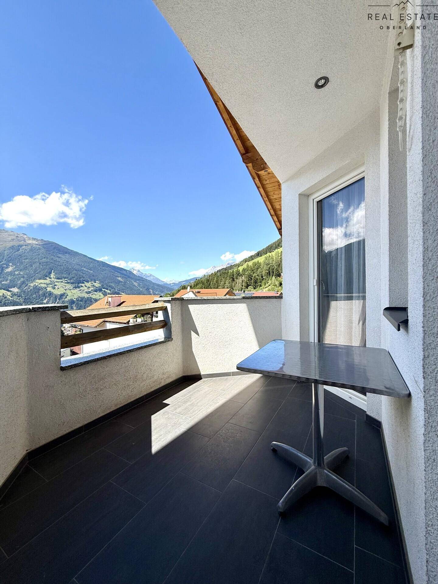 Sonniger Balkon mit kleinem Tisch und Stühlen, bietet einen weiten Bergblick und frische Luft.