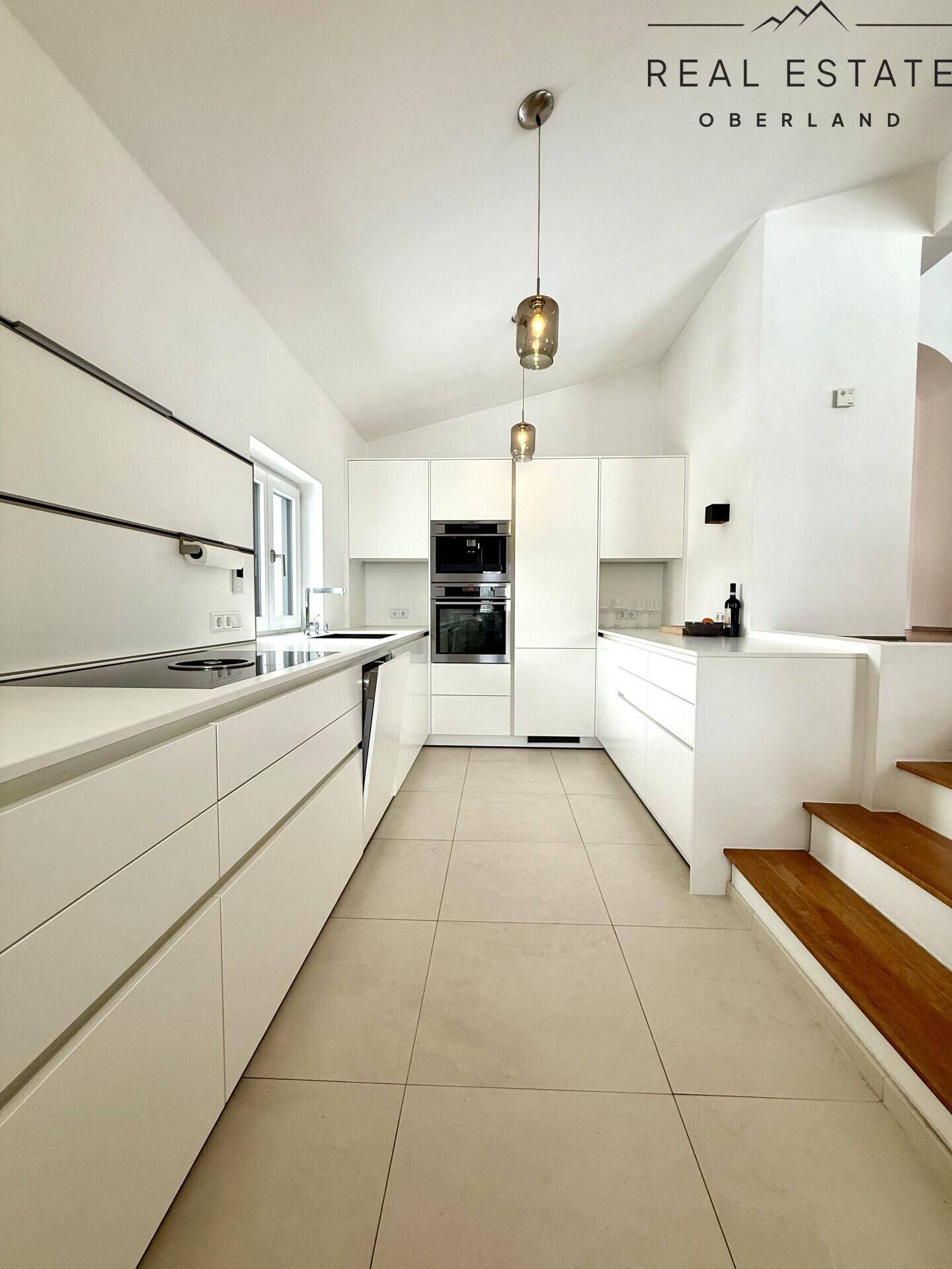 Helle, moderne Küche mit weißen Schränken, integriertem Backofen und Fenster.
