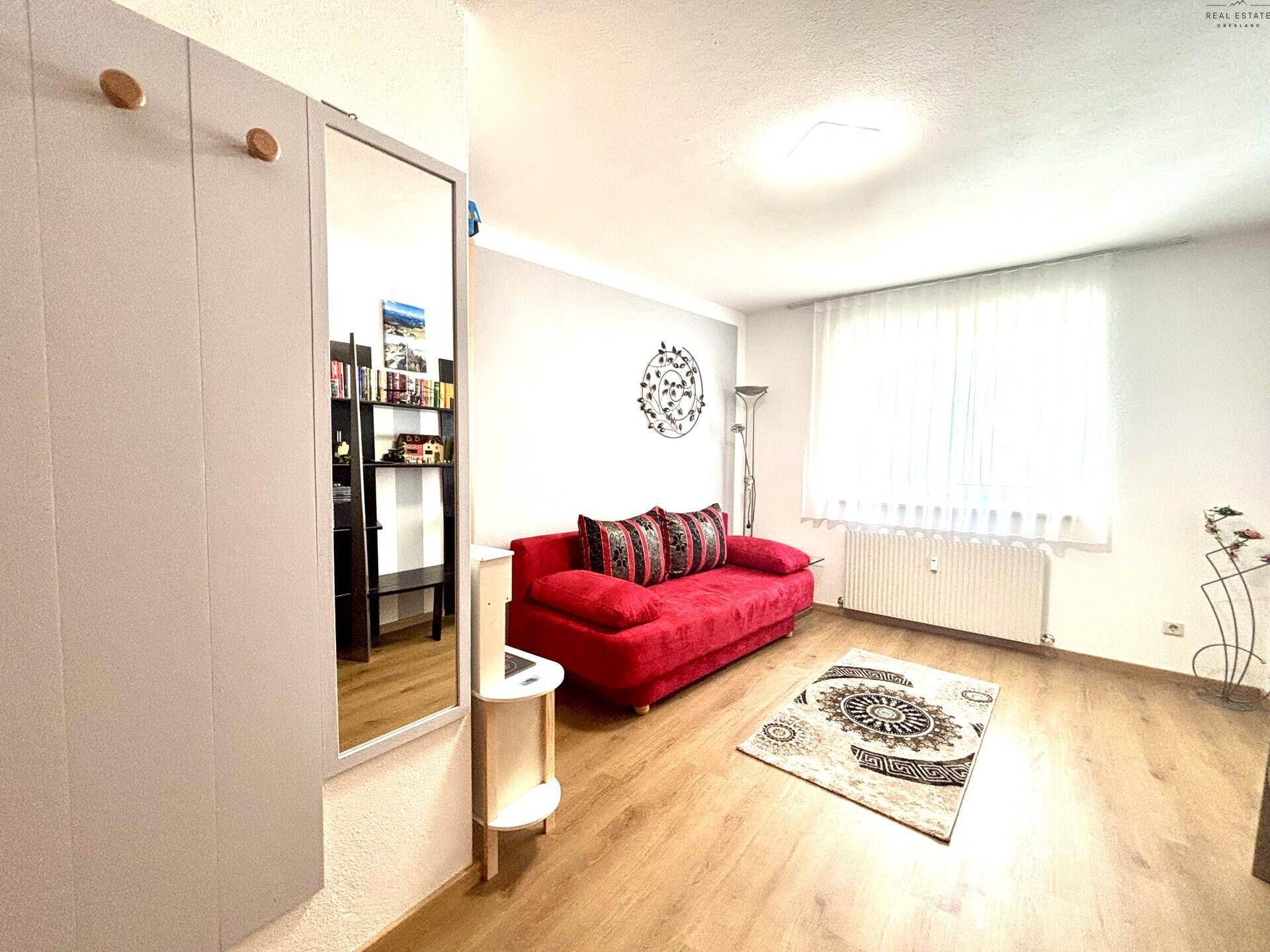 Gemütliches Zimmer mit rotem Sofa, Laminatboden und einem großen Spiegel, hell und einladend.