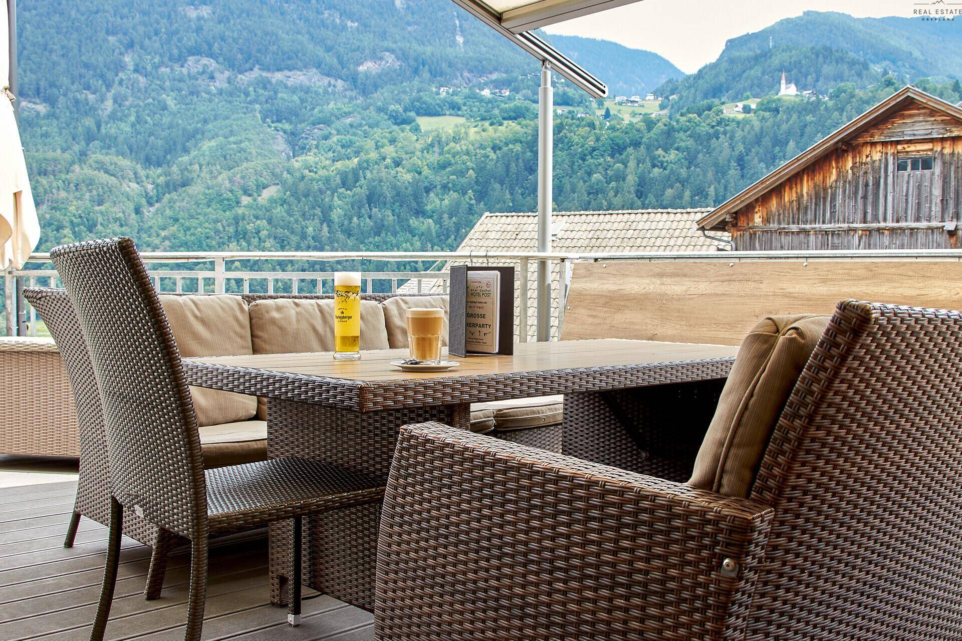Gemütliche Terrasse mit Rattanmöbeln, Esstisch und Panoramablick auf die grüne Berglandschaft.