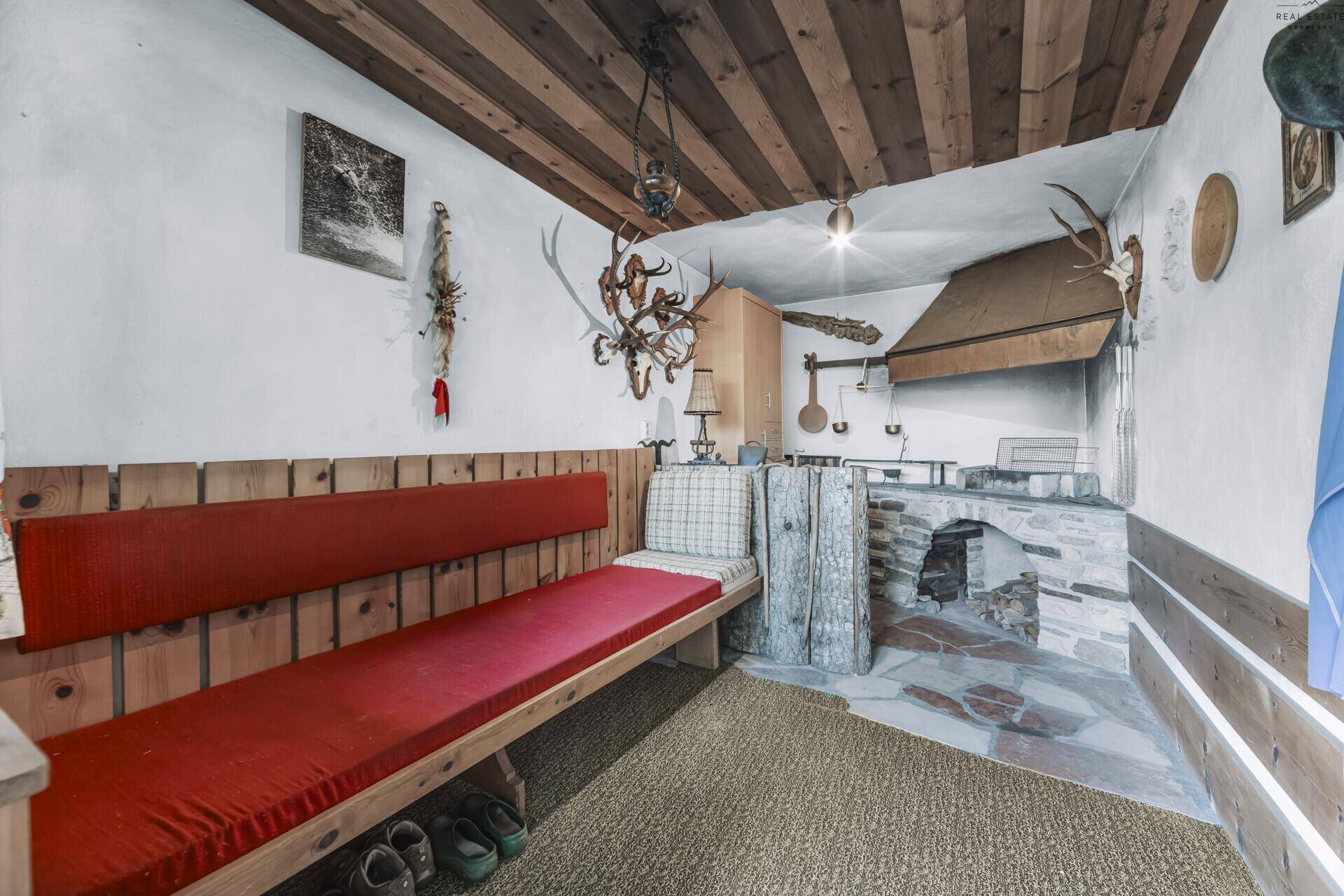 Rustikaler Raum im alpinen Stil mit Holzbänken, Kamin und Geweihdekoration.