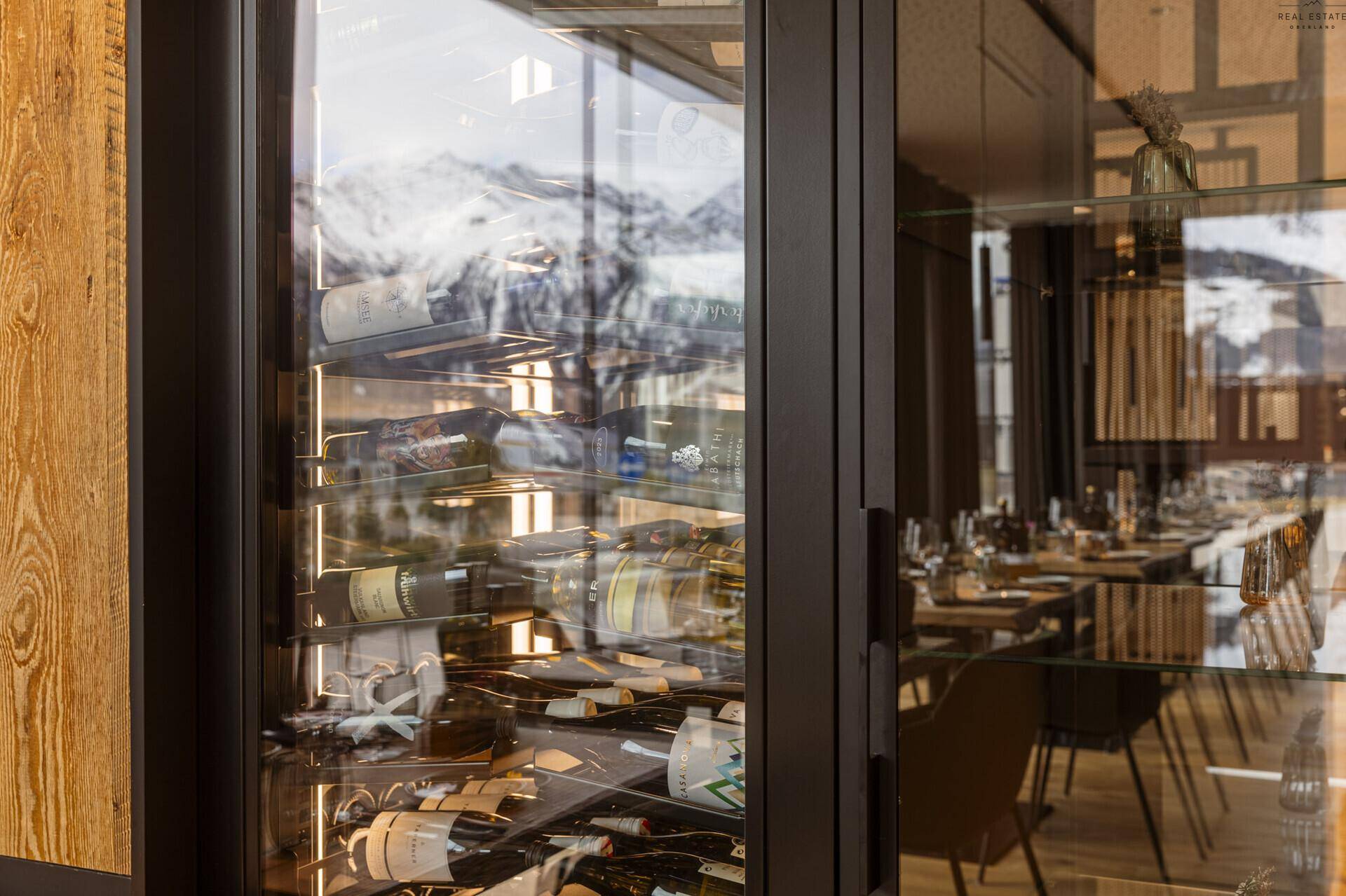 Weinkühlschrank mit zahlreichen Flaschen, der den Bergblick durch die Spiegelung der Fenster einfängt.