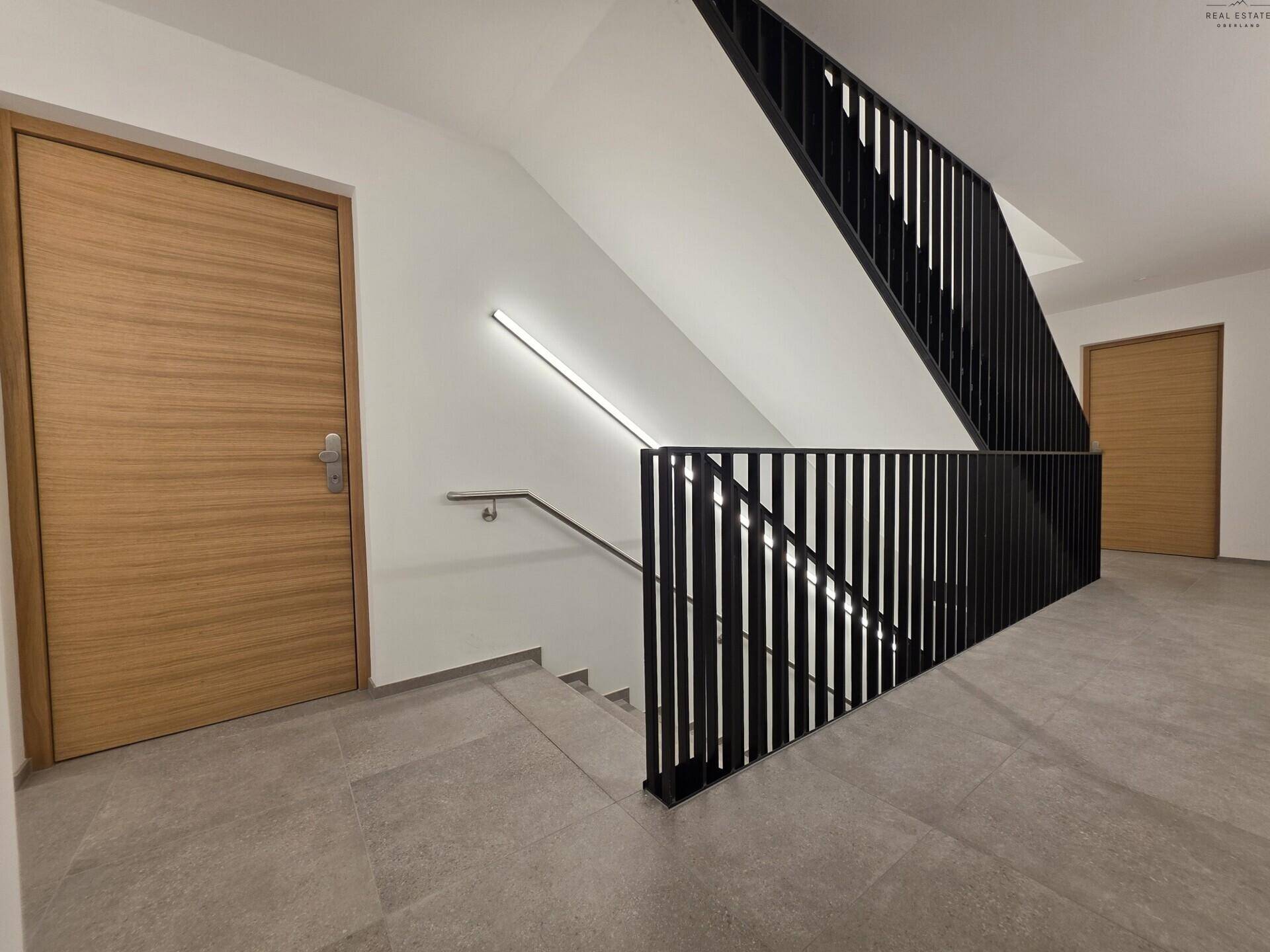 Modernes Treppenhaus mit schwarzem Geländer, Holztreppen und indirekter Beleuchtung.