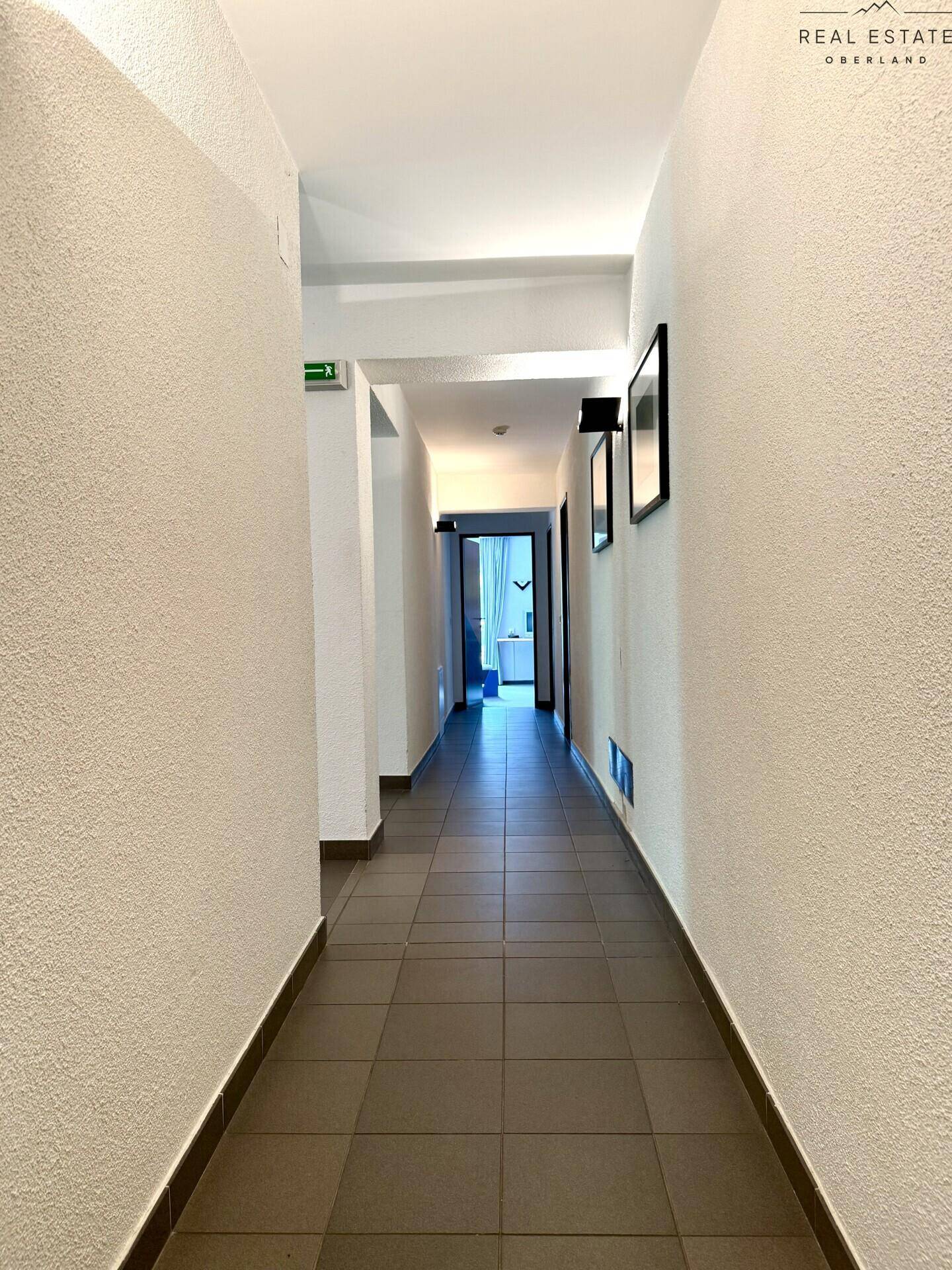 Langer, schmaler Flur mit Fliesenboden und weißen Wänden, der zu weiteren Räumen führt.