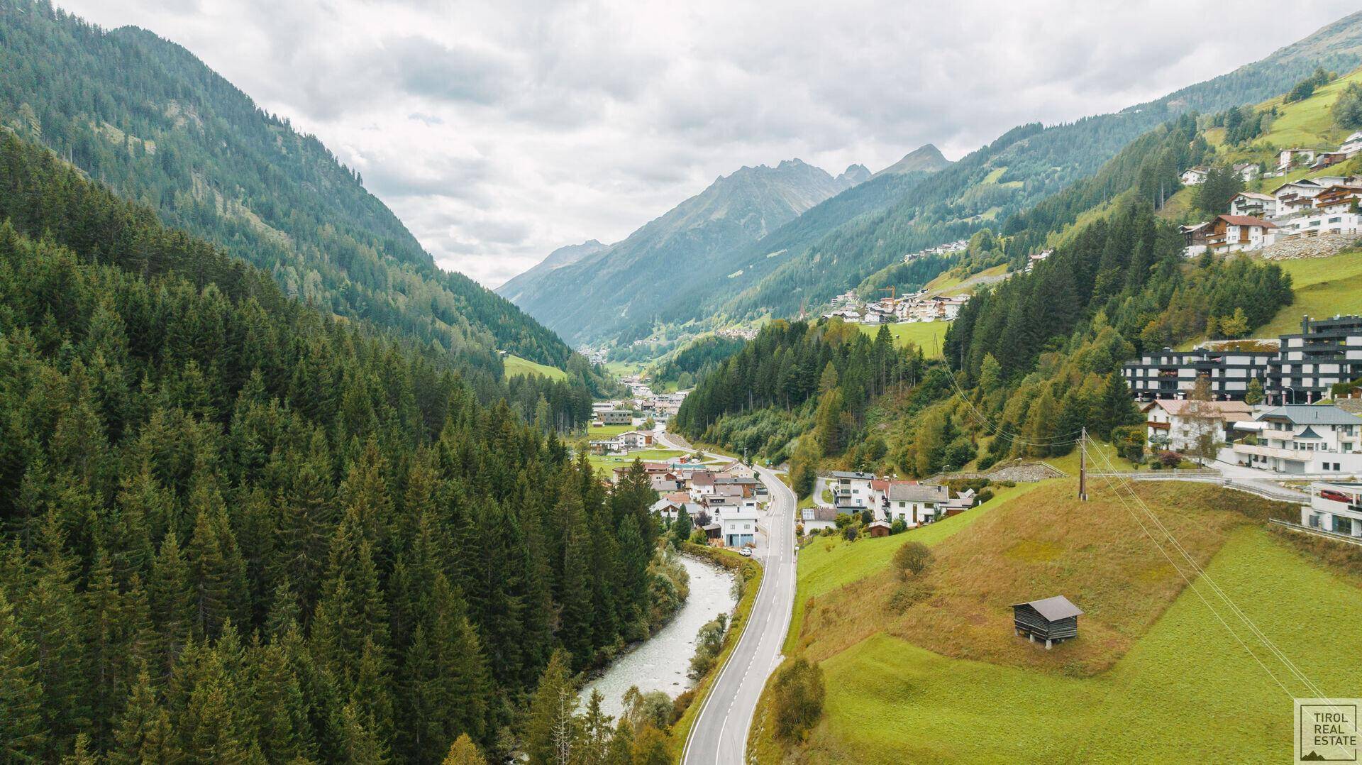 Panoramische Luftaufnahme eines weiten Tals mit Fluss, Straße, Dörfern und majestätischen Bergen im Hintergrund.