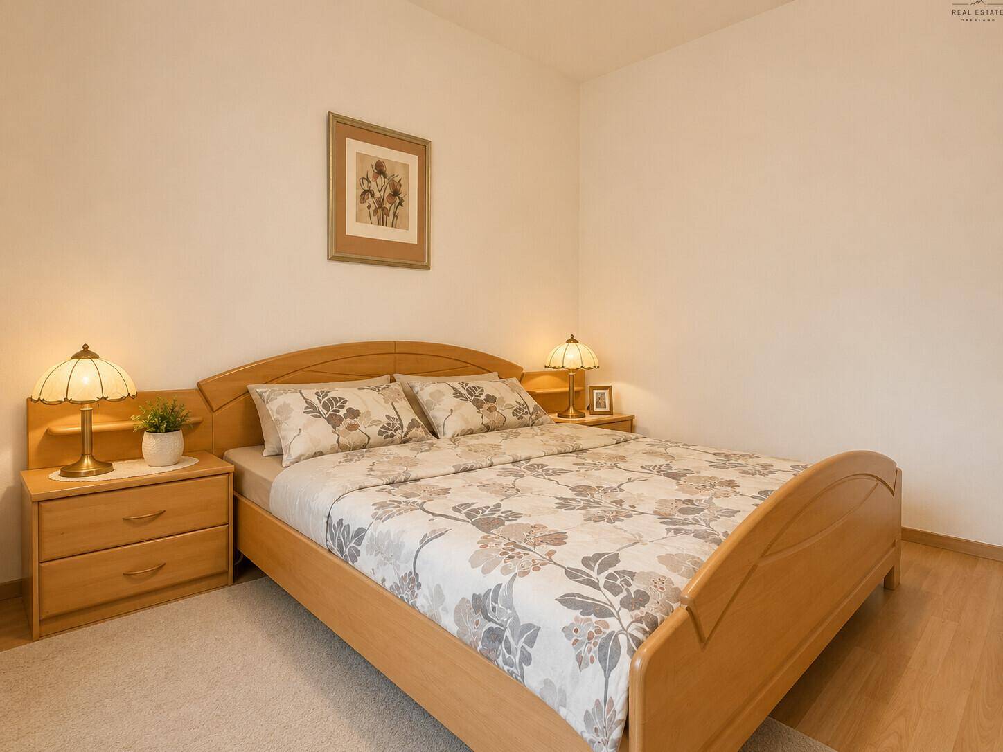 Schlafzimmer mit Doppelbett aus hellem Holz, Nachttischen und floral gemusterter Bettwäsche.