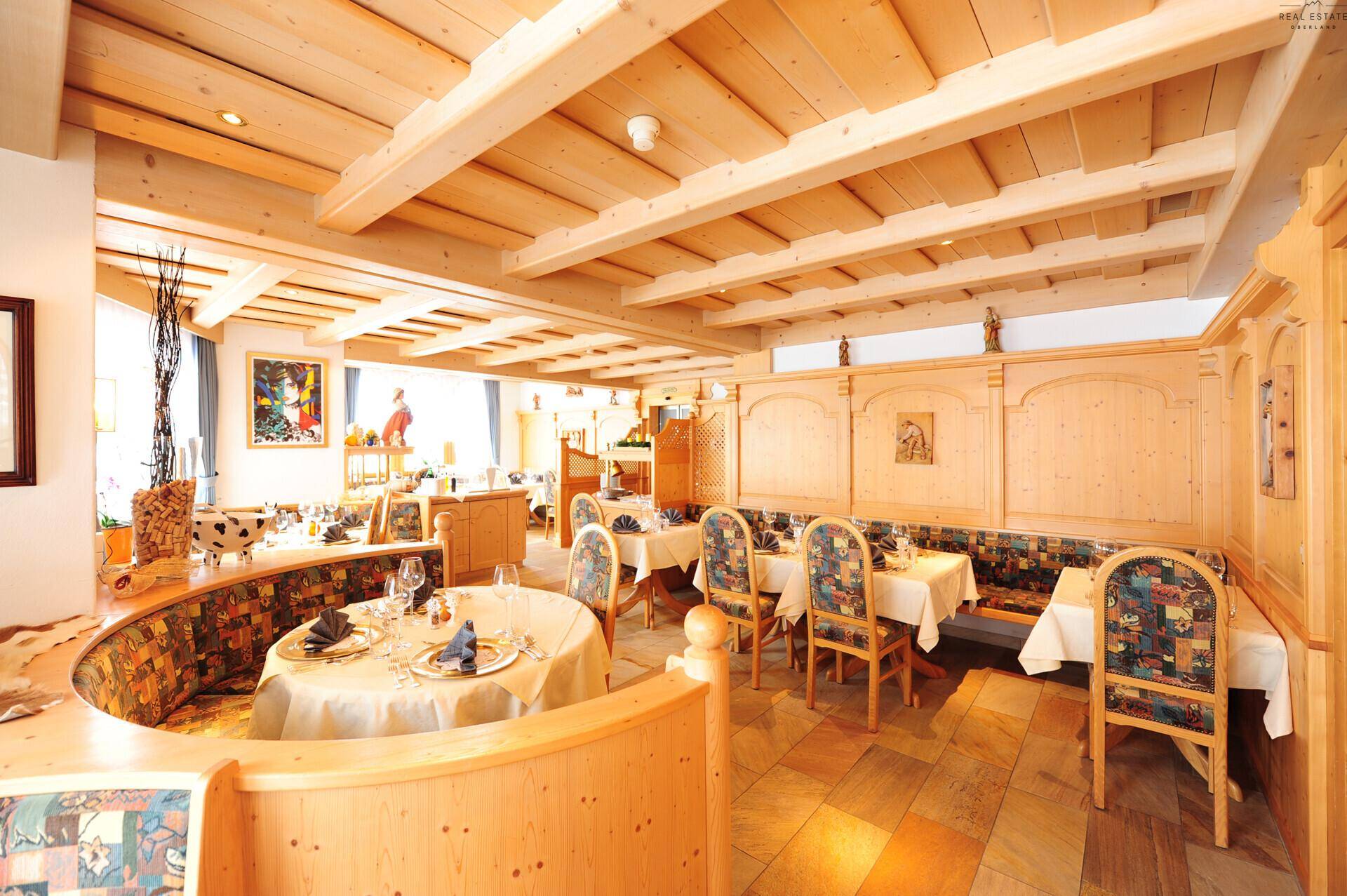 Traditioneller Speisesaal mit Holzbalkendecke, gemütlichen Sitzecken und elegant gedeckten Tischen.